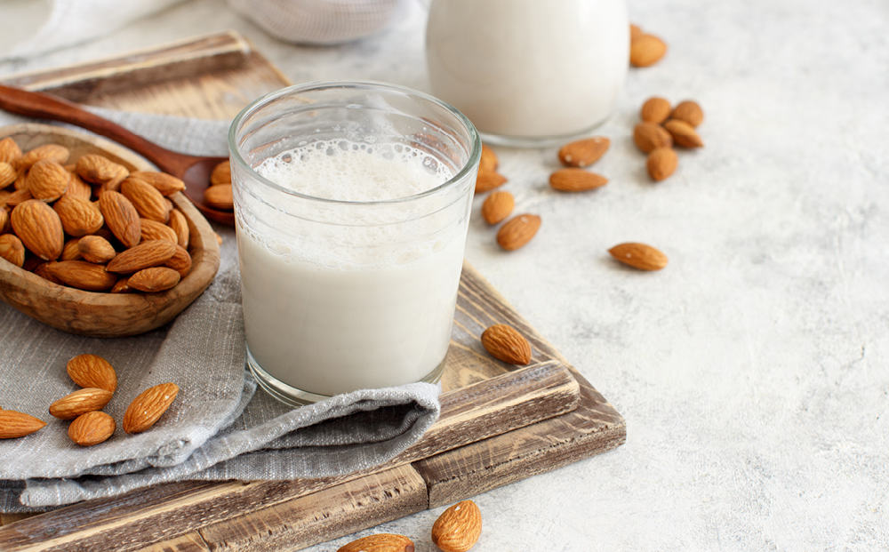 A glass of almond milk, with whole almonds scattered beside it.